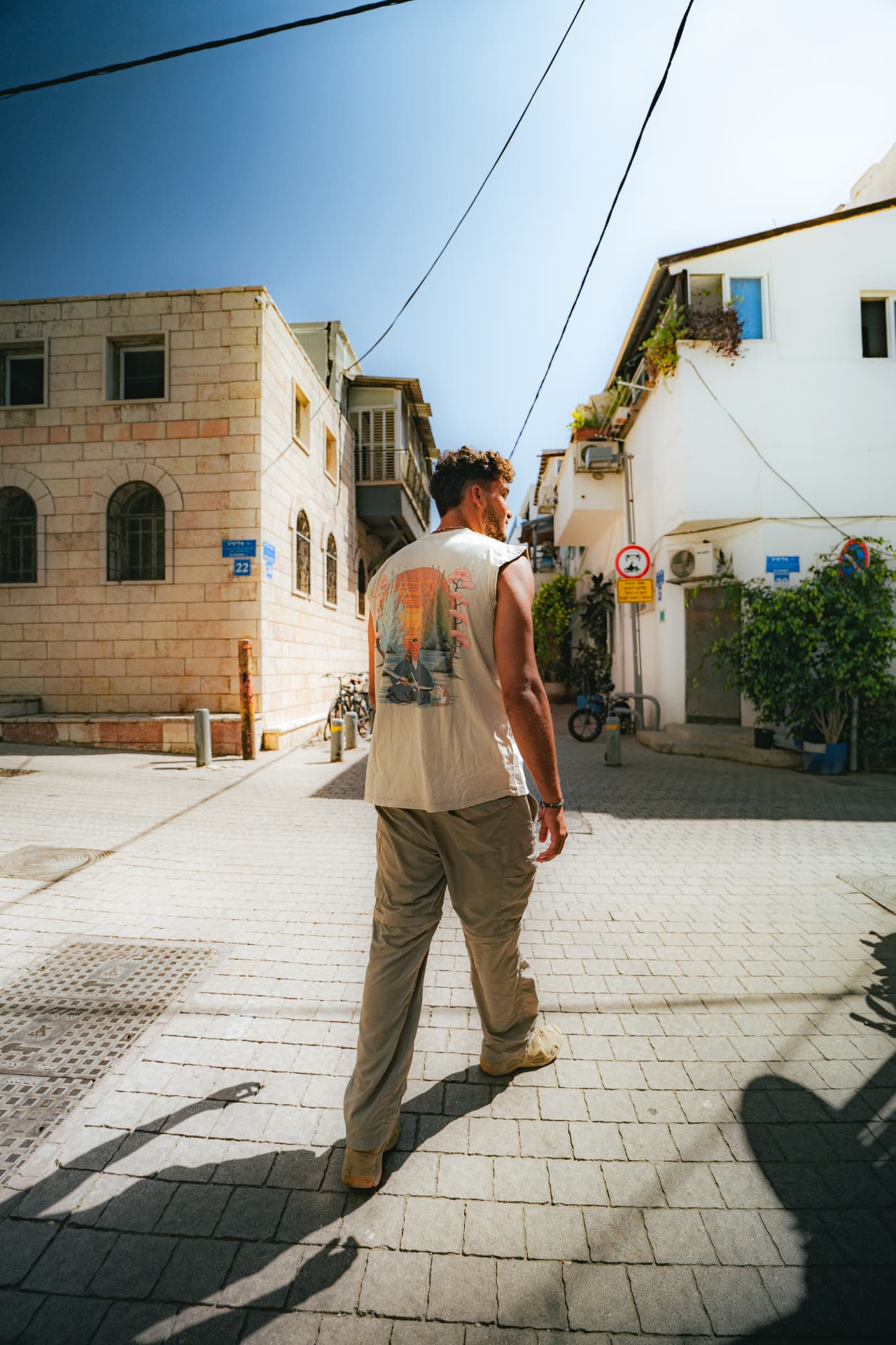בחור בגופייה מודפסת הולך בסמטה בנוה צדק באור יום